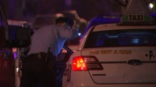 A Philadelphia police officer uses a flashlight to look into a taxi, where a driver was shot.