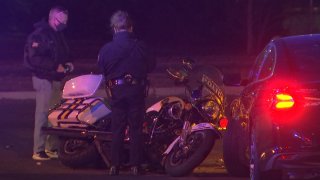 Two Philadelphia police detectives look on at a Philadelphia Highway Patrol motorcycle that rests on its side and is in front of a dark-colored sedan following a crash in which the officer on the motorcycle had to be hospitalized.