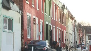 Brick row homes stand next to one another. A black sedan is parked in front of one of them.