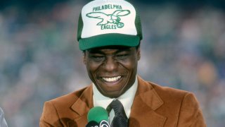 Analyst Irv Cross in an Eagles hat with a microphone