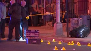 Several evidence markers are seen on the ground while investigators look on at the site of a shooting in Trenton, New Jersey.