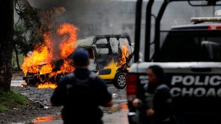 Fotografía de un vehículo incendiado, mientras dos policías ven cómo se quema