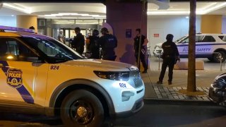 Police officers stand in front of the entrance to Thomas Jefferson University Hospital following a deadly shooting. The front of a police SUV can be seen parked in front of the officers and the hospital.