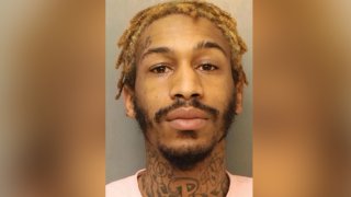Shafeeq Lewis stares ahead in a police mugshot. He sports a short beard, short, blond dreadlocks and several tattoos across his neck.