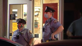 Two Philadelphia police officers in uniform wear face masks as they stand outside a Wawa store following a deadly shooting.