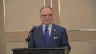 Moshe Porat in a blue suit standing at a podium