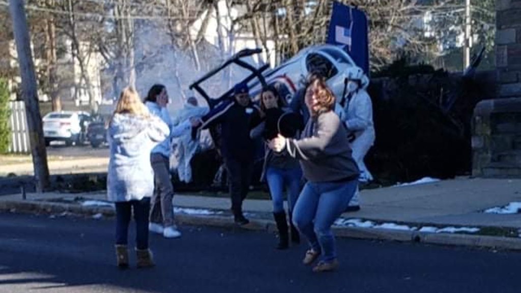 Multiple people stand around and run away as a helicopter crashes to the ground.