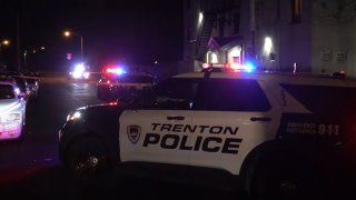 A Trenton Police Department SUV is parked in the foreground as other police vehicles flash their lights in the background.