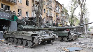 Los tanques se ven frente al edificio dañado mientras continúan los ataques rusos en Mariupol, Ucrania, mayo de 2022.