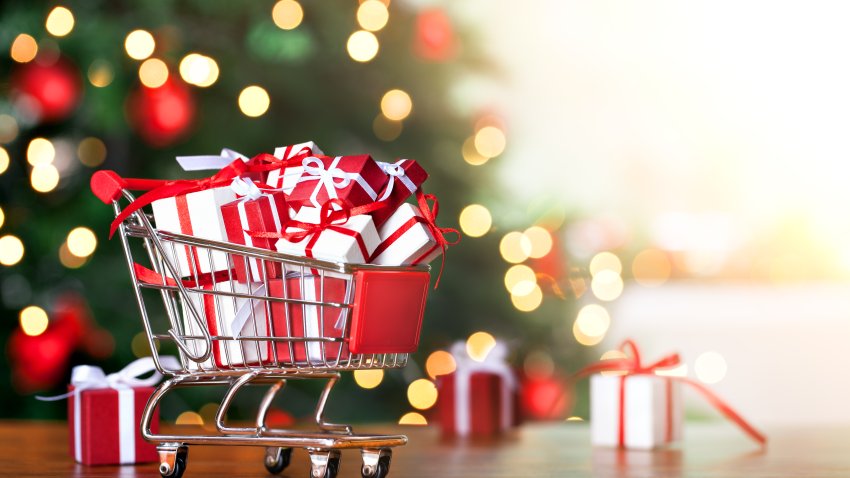 Little shopping cart full of christmas gifts on christmas tree background.