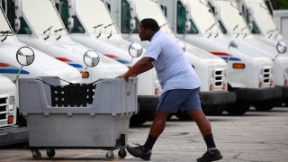 Un empleado del Servicio Postal de los Estados Unidos (USPS) pasa frente a varios vehículos de reparto en Louisville, Kentucky en julio de 2022.