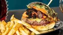 A cheeseburger made of eight ounces of wagyu beef topped with Wexford aged Irish Cheddar cheese, Italian Black Truffle, Italian Caviar and lobster meat, and features a bun topped with gold leaf is shown.