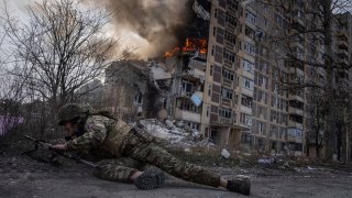 Un agente de la policía de Ucrania se pone a cubierto frente a un edificio en llamas, en Avdiivka, Ucrania, el 17 de marzo de 2023.