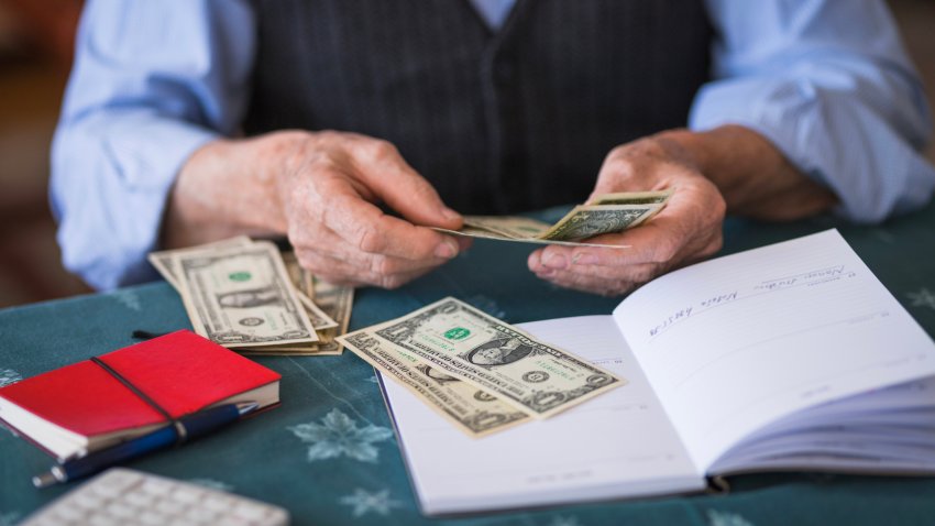 Elderly man counting dollar bills and taking notes about the expenses, close-up
