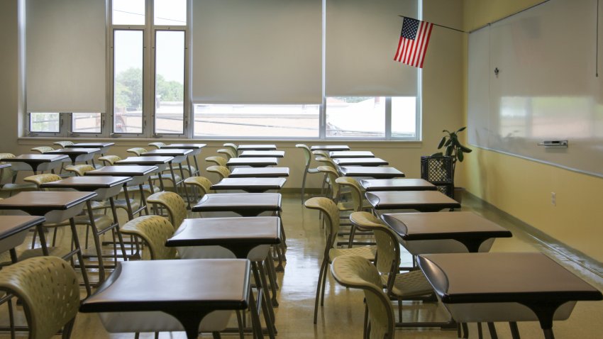 An empty classroom with rows of desks with the U.S. flag on wall.