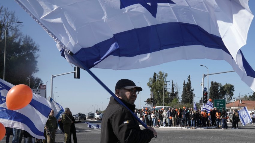 Israelíes esperan en la carretera el paso de la comitiva fúnebre de Shiri Bibas y sus dos hijos, Ariel and Kfir, que murieron durante su cautiverio en Gaza, cerca del kibbutz Yad Mordechai, en Israel, el 26 de febrero de 2025. (AP Foto/Maya Alleruzzo)